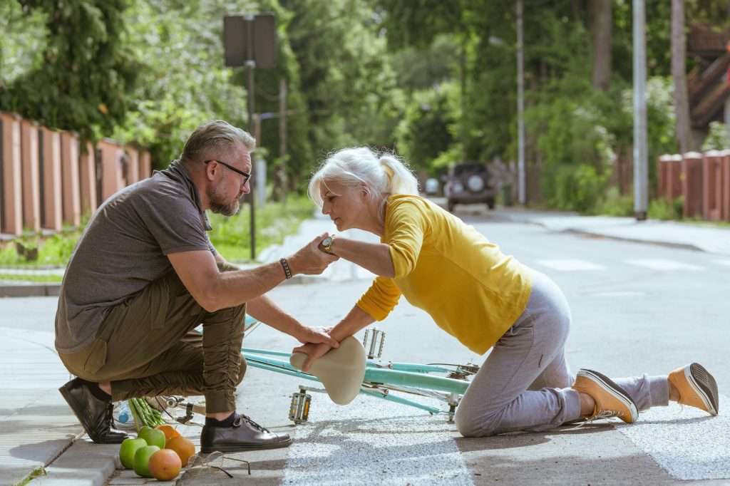 Handsome man helps an elderly woman get up after falling off a bicycle on a suburban road